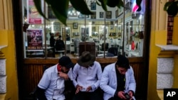 FILE - Barbers sit outside their workplace in the Yungay neighborhood of Santiago, Chile, June 6, 2024.