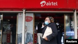 FILE - A woman speaks on her cellphone as she walks past a mobile phone service center operated by Kenyan's telecom operator Airtel Kenya in downtown Nairobi, Kenya, July 15, 2021.
