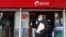 FILE - A woman speaks on her cellphone as she walks past a mobile phone service center operated by Kenyan's telecom operator Airtel Kenya in downtown Nairobi, Kenya, July 15, 2021.