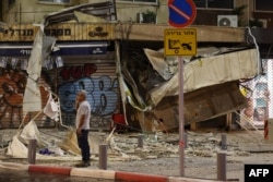 Muškarac stoji ispred oštećene prodavnice u Tel Avivu, nakon što je 7. oktobra 2023. pogođena raketom palestinskih militanata iz Pojasa Gaze.