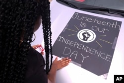 FILE - A woman decorates her car with a sign during a car parade to mark Juneteenth on Saturday, June 19, 2021, in Inglewood, Calif. (AP Photo/Ringo H.W. Chiu)