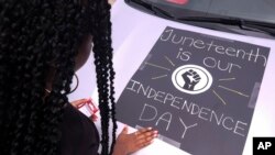 Seorang perempuan menghiasi mobilnya dengan poster untuk mengikuti parade Juneteenth, 19 Juni 2021, di Inglewood, California. (Foto: Ringo H.W.Chiu/AP Photo)