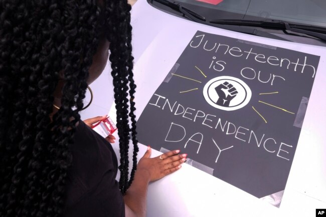 FILE - A woman decorates her car with a sign during a car parade to mark Juneteenth on Saturday, June 19, 2021, in Inglewood, Calif. (AP Photo/Ringo H.W. Chiu)