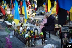 Relatives mourn over new graves of Ukrainian soldiers killed in recent battles as national and military units flags wave in a military cemetery in Lviv, Ukraine, April 23, 2023.