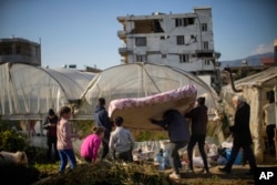 Sejumlah warga menggotong matras ke rumah kaca yang digunakan sebagai tempat pengungsian setelah gempa di Samandag, selatan Turki, 16 Februari 2023. (Foto: Francisco Seco/AP Photo)