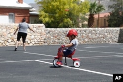 Dylan Park (3), berlatih mengendarai sepeda roda tiga di tempat parkir sementara orang tuanya bermain lempar frisbee di El Paso, Texas, 8 Mei 2020. (Cedar Attanasio/AP)