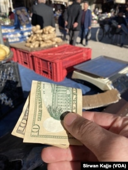 A buyer hands a U.S. $10 bill to a fruit and vegetable seller in Qamishli, Syria, March 26, 2024.