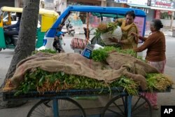 Preethi (kiri), menyerahkan sekarung sayuran kepada pelanggannya yang naik becak listriknya di Bengaluru, India, Senin, 10 Juli 2023. (AP/Aijaz Rahi)