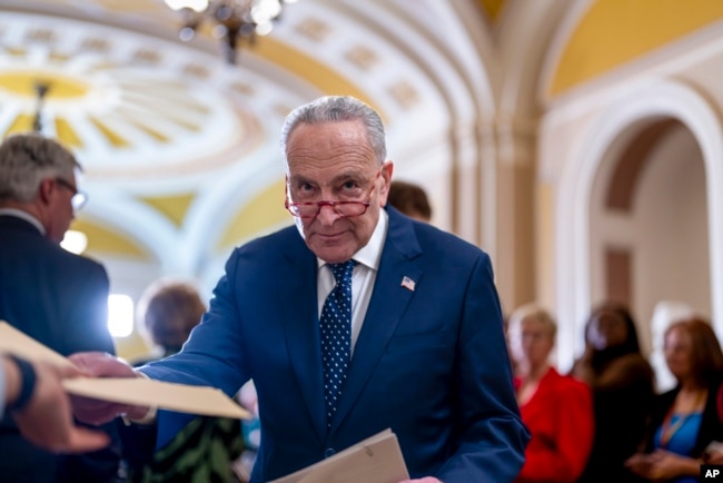 FILE - Senate Majority Leader Chuck Schumer, D-N.Y., hands papers to an aide as he talks with reporters about the struggle between Congress and the White House over the debt ceiling, at the Capitol in Washington, April 26, 2023.