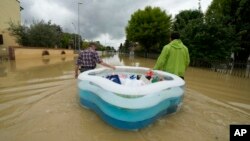 People use a plastic portable pool to carry bags and personal effects in a flooded road of Lugo, Italy, May 18, 2023.