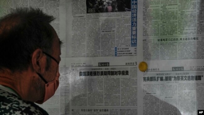 FILE - A man reads a Global Times article on investment curbs aimed at China, in Beijing, Aug. 10, 2023. China has accused Washington of trying to block its development via investment restrictions.