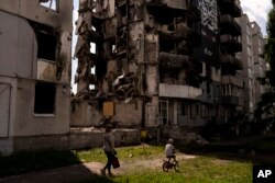 Una mujer y un niño pasan frente a un edificio de apartamentos destruido por ataques rusos en Borodyanka, Ucrania, el miércoles 2 de agosto de 2023. (Foto AP/Jae C. Hong)