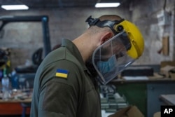 An engineer of "UkrPrototyp", sporting a Ukrainian flag on his shirt, works on new parts for a ground drone, in northern Ukraine, Thursday, June 27, 2024. (AP Photo/Anton Shtuka)