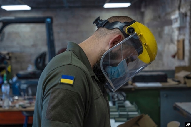 An engineer of "UkrPrototyp", sporting a Ukrainian flag on his shirt, works on new parts for a ground drone, in northern Ukraine, Thursday, June 27, 2024. (AP Photo/Anton Shtuka)