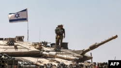 Israeli army soldiers stand atop the turret of a tank positioned in southern Israel near the border with the Gaza Strip on May 9, 2024.