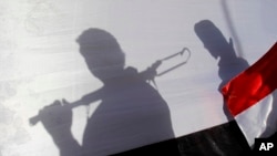 FILE - The shadow of Shiite rebels, known as Houthis, are cast on a large representation of the Yemeni flag as they attend a demonstration against an arms embargo imposed by the UN Security Council on Houthi leaders, in Sanaa, Yemen, on April 16, 2015. 