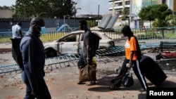 Students walk with their suitcases as they pass burned-out cars, at the gates of the Cheikh Anta Diop University of Dakar, following violent protests, June 2, 2023.