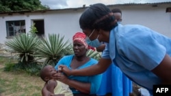 Msaidizi wa masuala ya Afya Ester Lunga (kulia) akitoa dozi ya chanjo ya polio kwa mtoto katika kitongoji cha Chilinde kilichopo katika mji wa Lilongwe Malawi, Machi 21, 2022. Picha na Amos Gumulira / AFP.