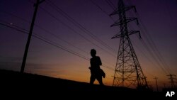 A jogger passes power lines during a sunset run, Aug. 20, 2023, in San Antonio. Triple-digit temperatures continue to stress the state's power grid.