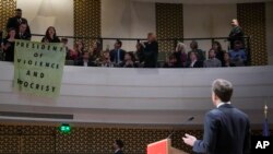 French President Emmanuel Macron, right, looks at demonstrators unfolding a banner that says "President of Violence and Hypocrisy" while he explains his vision of Europe during a lecture in The Hague, Netherlands, April 11, 2023.