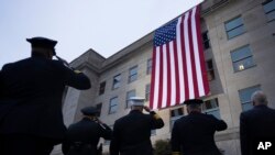 Працівники служб надзвичайних ситуацій віддають салют американському прапору, вивішеному на Пентагоні на сході сонця на честь терористичного нападу на Пентагон у 2001, 11 вересня 2023 року. 