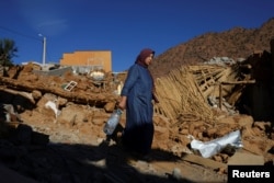 A woman carries a bottle, as she walks near rubble, in the aftermath of a deadly earthquake, in a hamlet on the outskirts of Talat N'Yaaqoub, Morocco, Sept. 11, 2023.