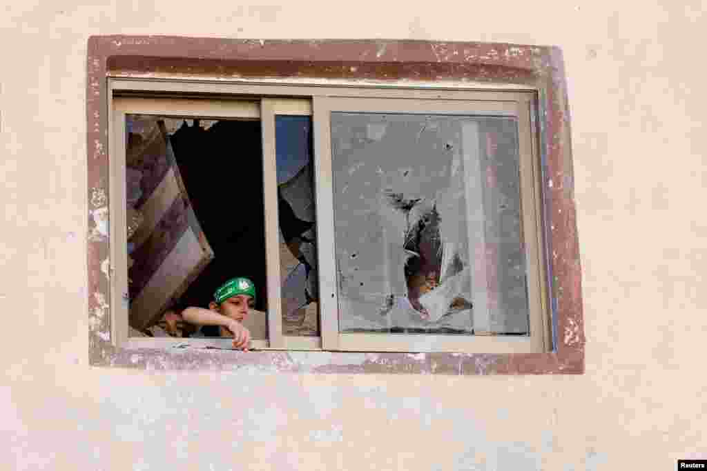 A Palestinian boy wearing the headband of Qassam brigades, the armed wing of Hamas, looks out of a damaged window with another child during an Israeli raid, in Tubas, in the Israeli-occupied West Bank.