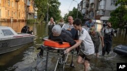 Volunteers haul a woman on a stretcher as she was being evacuated from a flooded neighborhood of the left bank of the Dnipro River, in Kherson, Ukraine, June 9, 2023.
