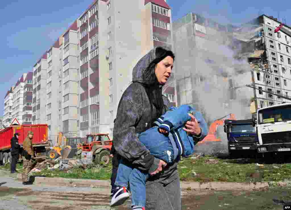 A woman walks past damaged residential buildings as she carries a child in Uman, Ukraine, after Russian missile strikes targeted several Ukrainian cities overnight.