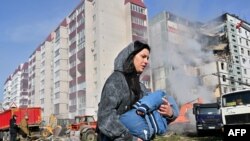 在乌克兰中部城镇乌曼，一名妇女抱着孩子走过被俄罗斯导弹击中的居民楼。(2023年4月28日)