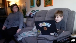 Jessica Blalack, left, watches as her son Phoenix Blalack, 6 , works with a tutor on his laptop in his Indianapolis home, Tuesday, March 7, 2023. (AP Photo/AJ Mast)