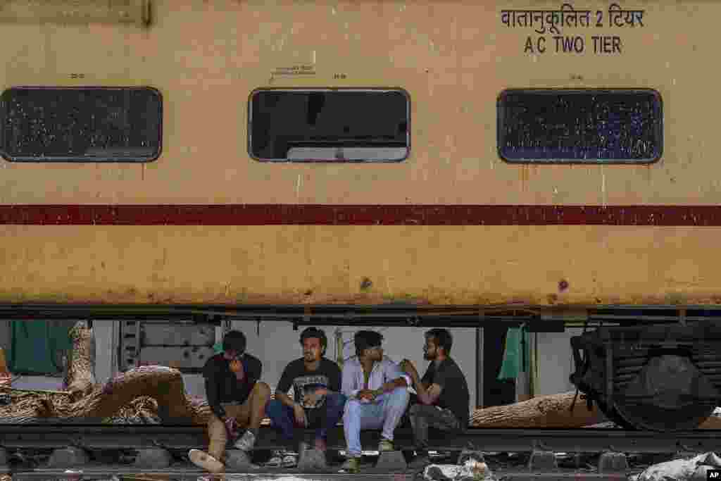 People sit and chat in the shade beneath a stationary train coach on a hot summer day in Mumbai, India.