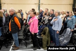 FILE - People stand and recite the pledge of allegiance at a caucus site in Clive, Iowa, Jan. 15, 2024. (AP Photo/Andrew Harnik, File)