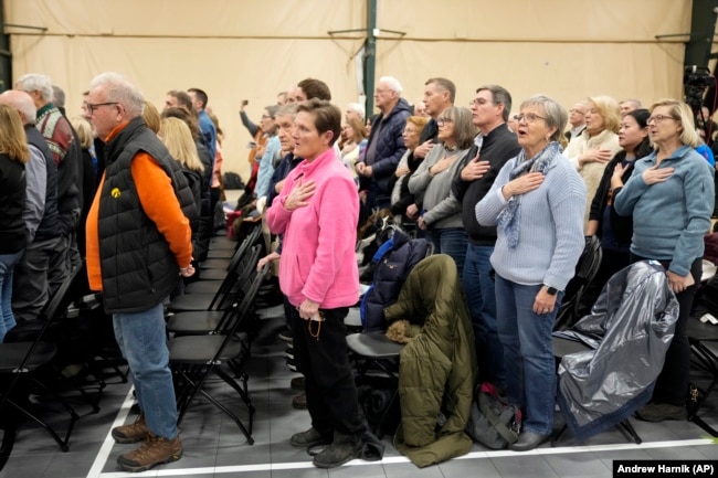 FILE - People stand and recite the pledge of allegiance at a caucus site in Clive, Iowa, Jan. 15, 2024. (AP Photo/Andrew Harnik, File)