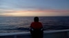 FILE - Somali migrant Amsa, 16, last name not available, watches the sunset as he stands aboard a ferry leaving the Sicilian Island of Lampedusa, Oct. 7, 2013. 
