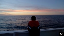 FILE - Somali migrant Amsa, 16, last name not available, watches the sunset as he stands aboard a ferry leaving the Sicilian Island of Lampedusa, Oct. 7, 2013. 