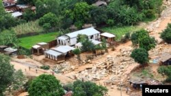 FILE - People walk by houses damaged by Tropical Cyclone Freddy, around 100 km outside Blantyre, Malawi, March 18, 2023. 