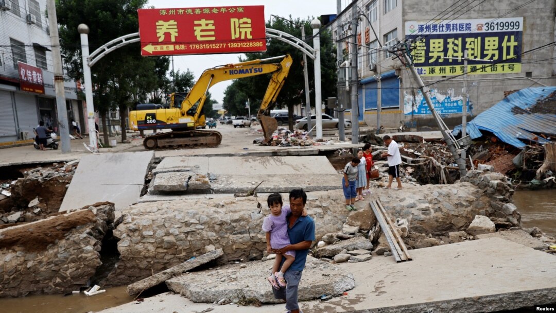 Seorang pria menggendong seorang anak berjalan melintasi jembatan yang rusak setelah hujan dan banjir akibat sisa-sisa Topan Doksuri, di Zhuozhou, Provinsi Hebei, China, 7 Agustus 2023. (REUTERS/Tingshu Wang)
