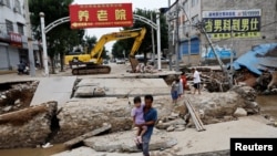 Seorang pria menggendong seorang anak berjalan melintasi jembatan yang rusak setelah hujan dan banjir akibat sisa-sisa Topan Doksuri, di Zhuozhou, Provinsi Hebei, China, 7 Agustus 2023. (REUTERS/Tingshu Wang)