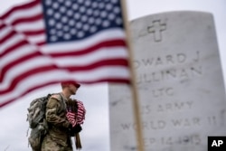 A member of the 3rd U.S. Infantry Regiment also known as The Old Guard, places flags in front of each headstone for "Flags-In" at Arlington National Cemetery in Arlington, Thursday, May 25, 2023, to honor the Nation's fallen military heroes ahead of Memorial Day. (AP Photo/Andrew Harnik)