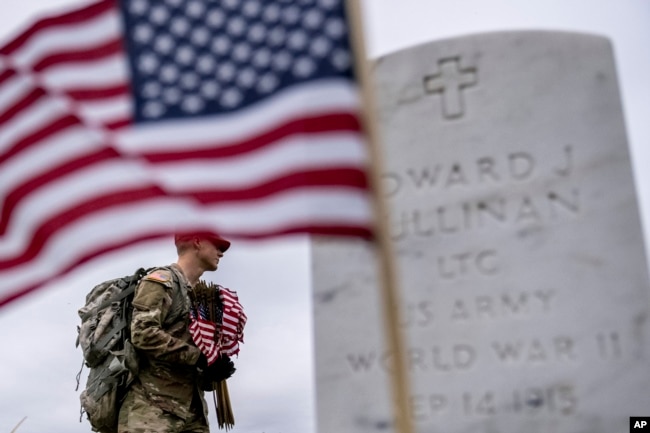 A member of the 3rd U.S. Infantry Regiment also known as The Old Guard, places flags in front of each headstone for "Flags-In" at Arlington National Cemetery in Arlington, Thursday, May 25, 2023, to honor the Nation's fallen military heroes ahead of Memorial Day. (AP Photo/Andrew Harnik)