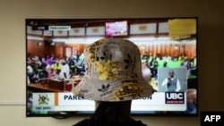 A Ugandan transgender woman who was recently attacked and currently being sheltered watches a TV screen showing the live broadcast of the session from the Parliament for the anti-gay bill near Kampala on March 21, 2023.