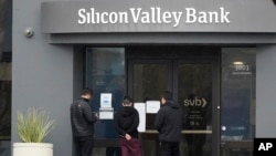 FILE - People look at signs posted outside an entrance to Silicon Valley Bank in Santa Clara, California, March 10, 2023. 