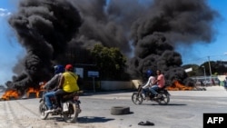 FILE - Motorcyclists drive by burning tires during a police demonstration after a gang attack on a police station that left six officers dead, in Port-au-Prince, Haiti, Jan. 26, 2023.