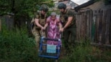 Police officers of the White Angels unit help a woman in the Donetsk region of Ukraine evacuate to a safe area, June 28, 2024. On Saturday, Russian forces fired missiles outside Zaporizhzhia, killing seven people, including two children.