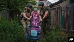 Police officers of the White Angels unit help a woman in the Donetsk region of Ukraine evacuate to a safe area, June 28, 2024. On Saturday, Russian forces fired missiles outside Zaporizhzhia, killing seven people, including two children.