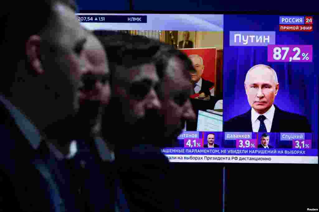 Men sit near a TV broadcasting news on the results of Russian presidential candidate and incumbent President Vladimir Putin, on the final day of the presidential election in Moscow, March 17, 2024. 