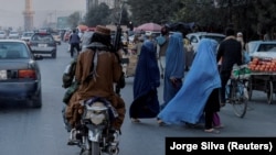 (FILE) A group of women wearing burqas crosses the street as Taliban members drive past in Afghanistan.