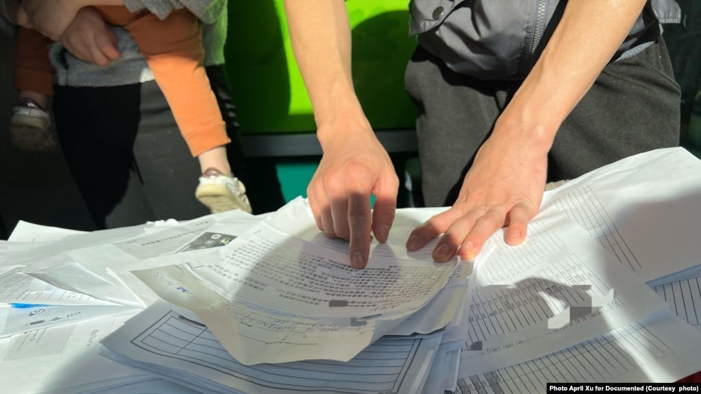 A victim points to a thick pile of paper documenting the victims who want to report the Ponzi scheme. Photo: April Xu for Documented(photo:VOA)