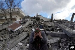 FILE - A woman sits on the rubble as emergency rescue teams search for people under the remains of destroyed buildings in Nurdagi town on the outskirts of Osmaniye city southern Turkey, on Feb. 7, 2023.